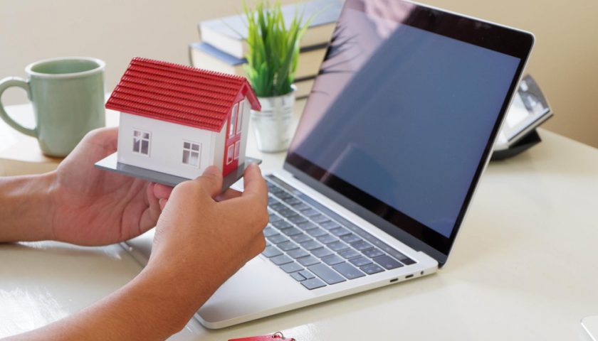 une personne tient une maquette de maison devant un ordinateur
