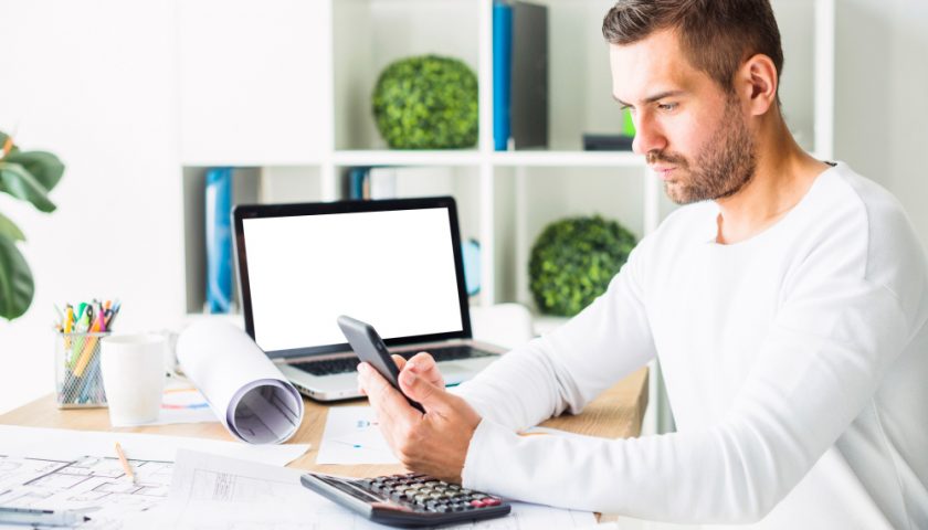 une homme regardant son téléphone et assis sur son bureau de travail